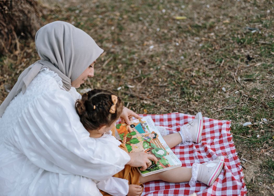 Madre e hija leyendo juntas un libro sobre una manta en el exterior