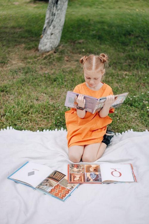 Niña leyendo un libro sentada sobre una manta en el parque